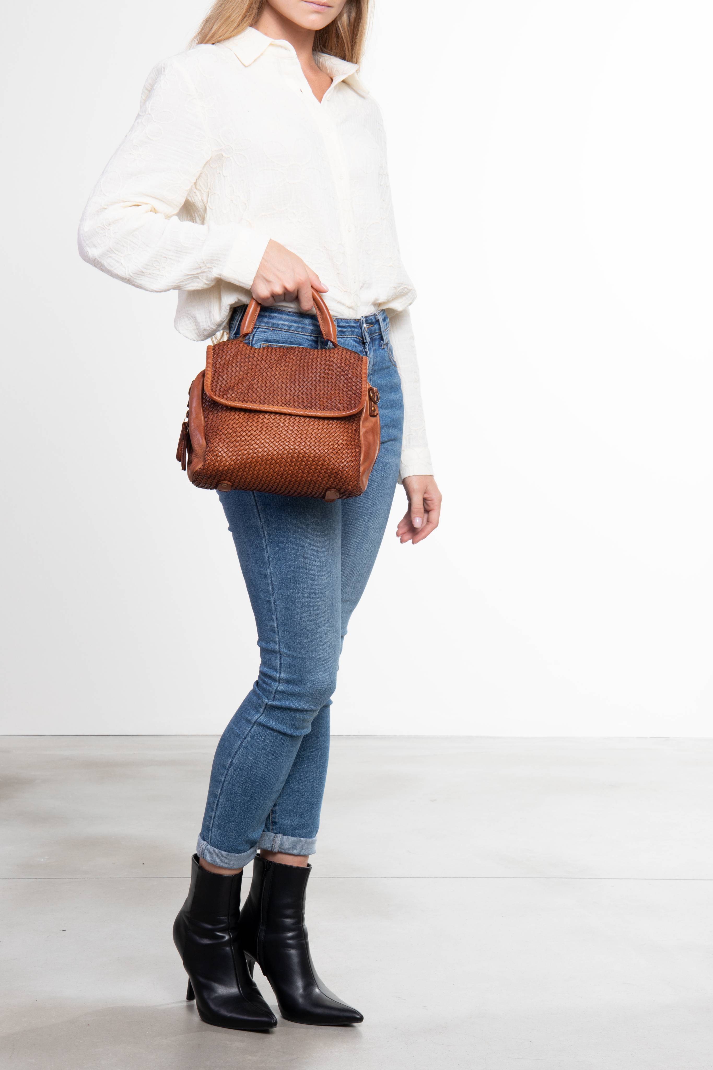 Donna in piedi che tiene una borsa a mano in pelle intrecciata colore cuoio