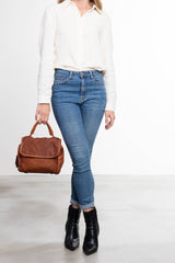 Donna con gambe incrociate che tiene una borsa a mano in pelle intrecciata colore cuoio