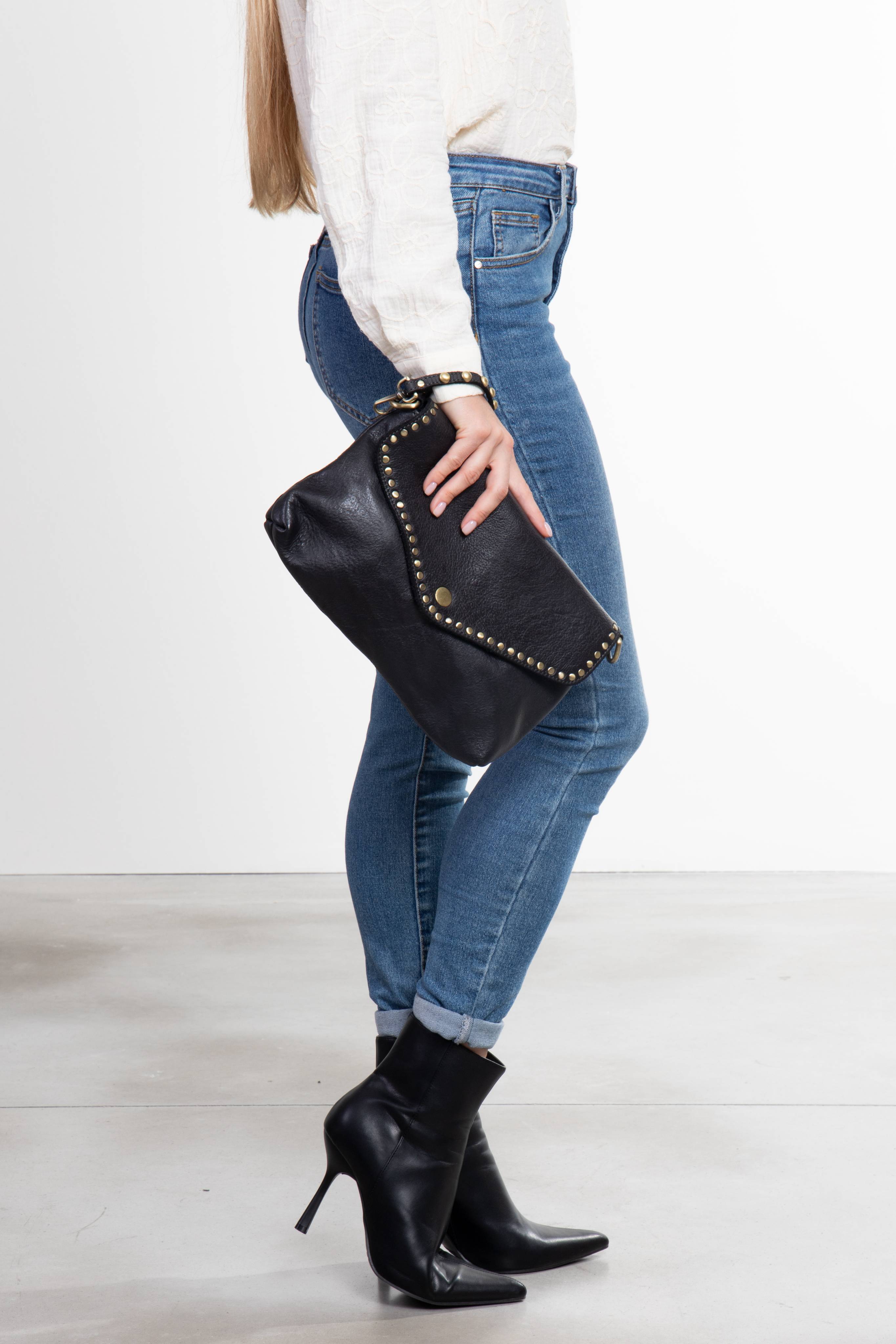 Donna in posa laterale che tiene La Busta, pochette donna in pelle nera con borchie