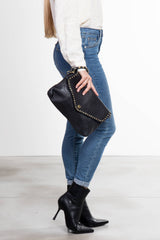 Donna in posa laterale che tiene La Busta, pochette donna in pelle nera con borchie