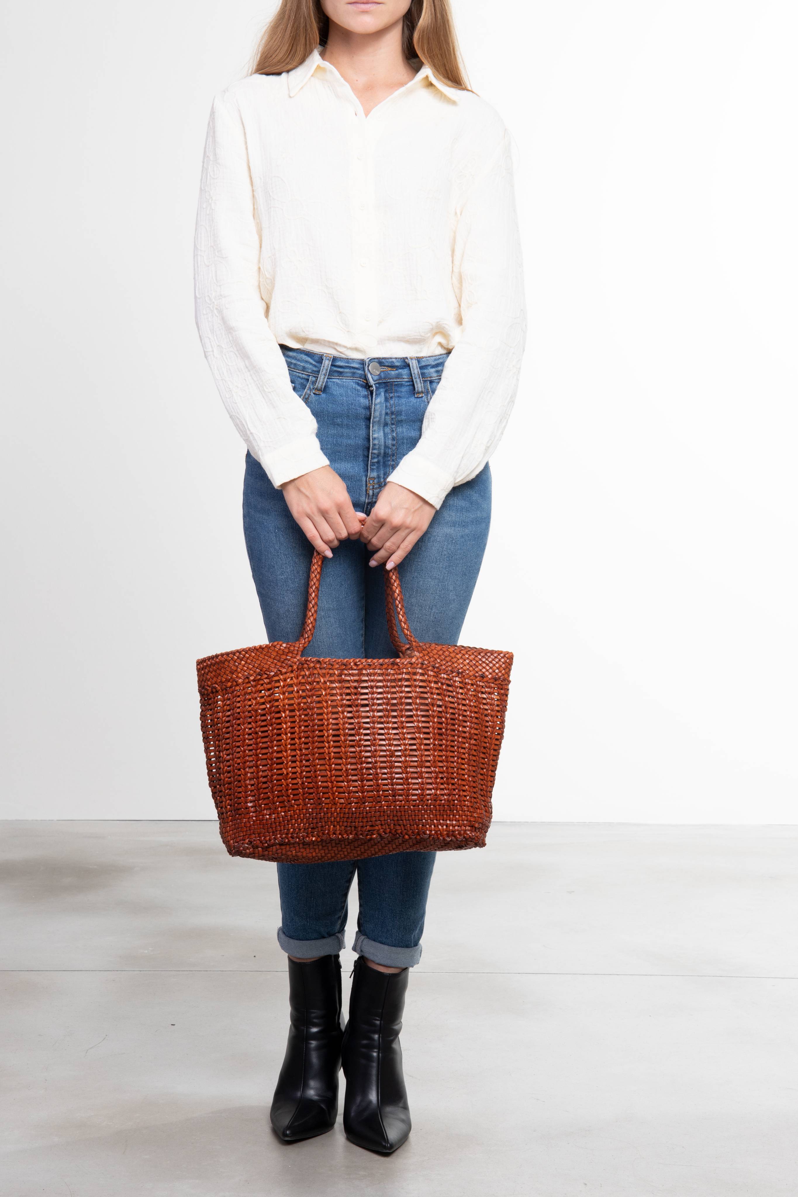 Donna che tiene in mano la borsa tote intrecciata La Toscana in pelle color cuoio