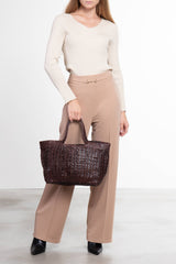 Donna che tiene in mano la borsa tote intrecciata La Toscana in pelle marrone
