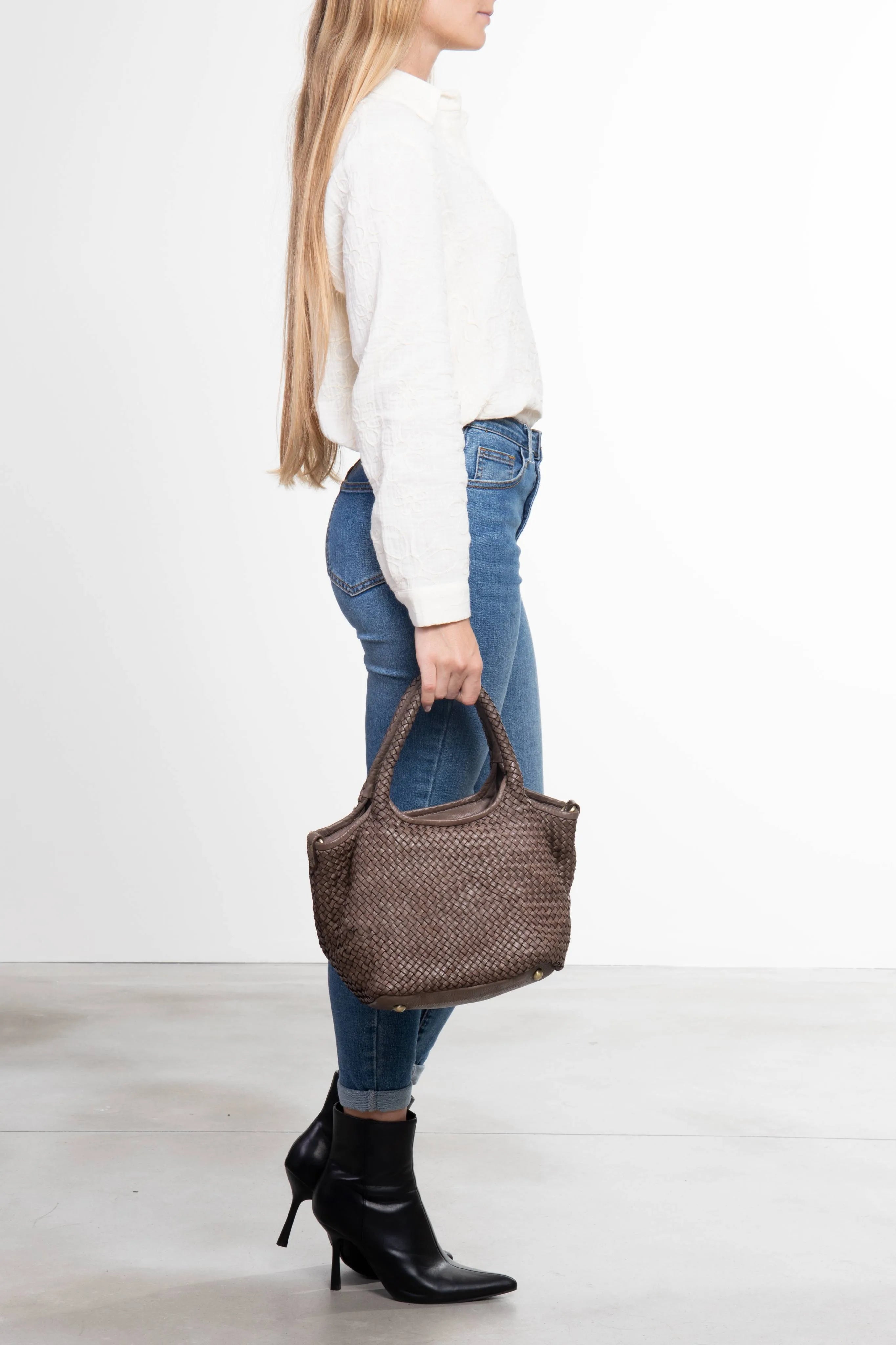 Donna che tiene la borsa tote Tuscan Weave in pelle intrecciata colore taupe vista laterale